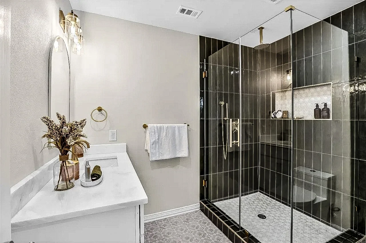 Walk-in shower with glossy black tile, brass fixtures and frameless glass in a completed Lakewood, Dallas renovation.