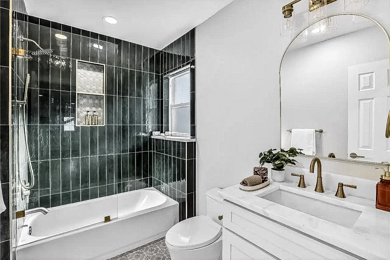 Bathroom with deep green glossy tile, a brass filler tap, white vanity and arched mirror in a completed Lakewood, Dallas remodel.