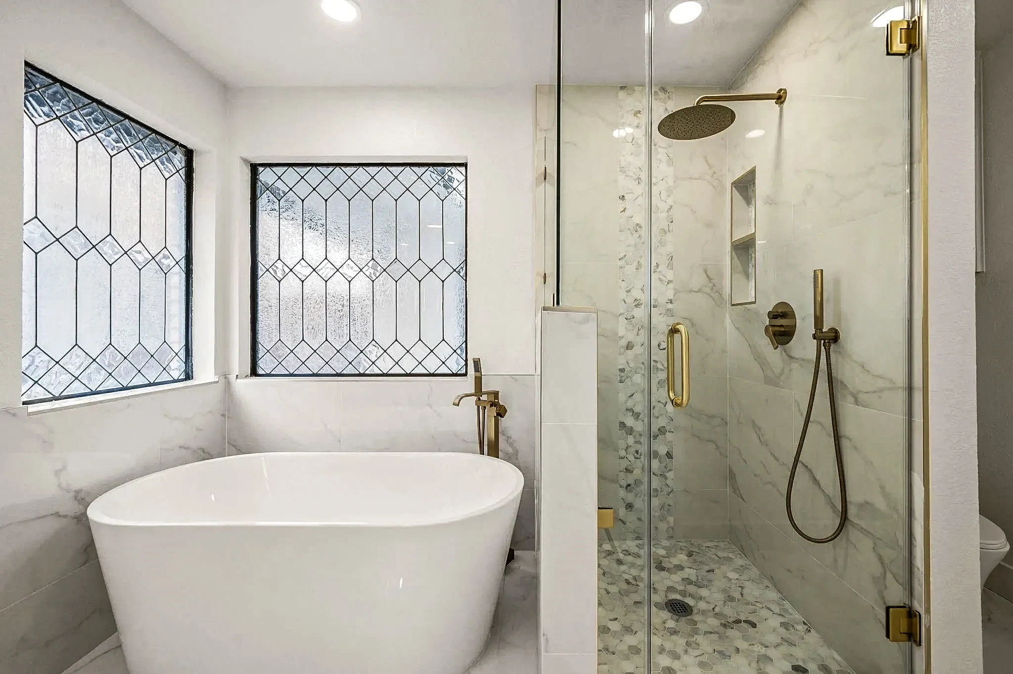 Primary wet room with a freestanding tub, marble-look shower, leaded window and brass fixtures in a completed Grapevine, Texas whole-home remodel.