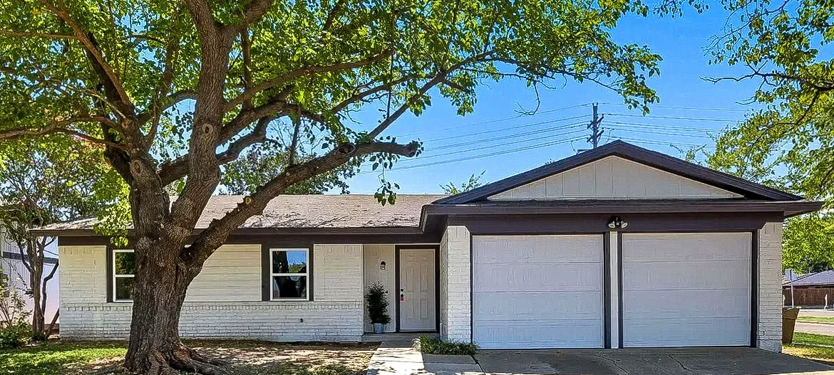 Freshly painted white Lewisville exterior with black trim, a three-car garage, large shade tree, and updated entry in Lewisville, Texas.
