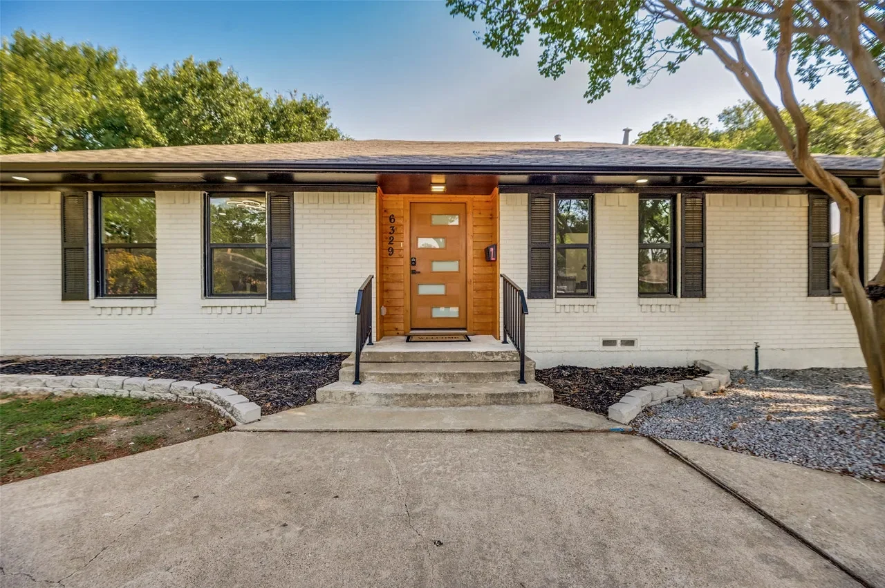 White brick Lower Greenville home with black replacement windows, modern wood entry door, and refreshed front landscaping in Lower Greenville, Dallas, Texas.