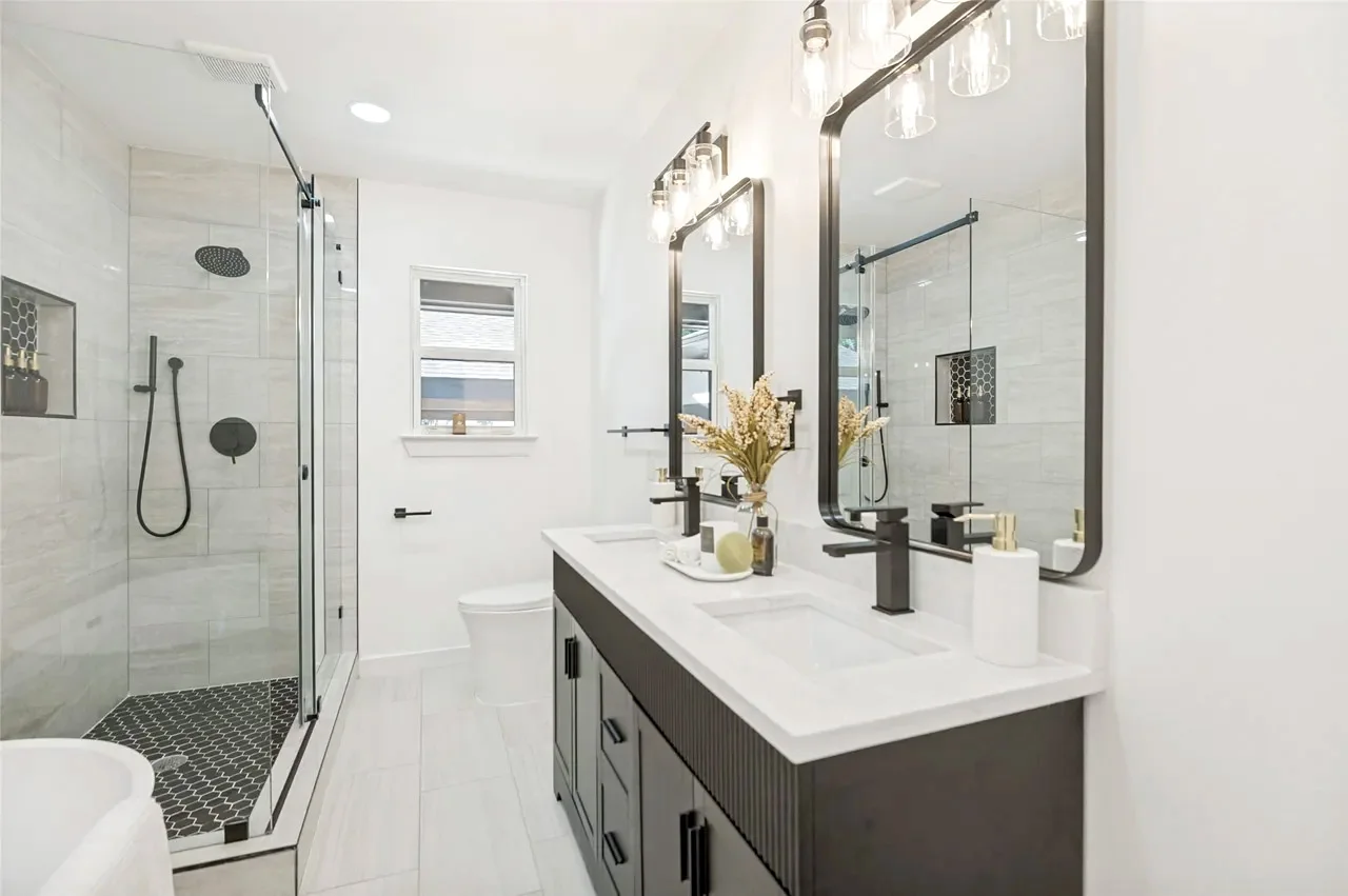 Primary bathroom with a glass wet room, rain shower, dark double vanity, white counters, and black fixtures in Lower Greenville, Dallas, Texas.
