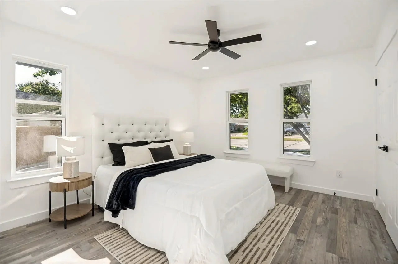 Secondary bedroom with white walls, wood-look flooring, black ceiling fan, three windows, and staged furnishings in Lower Greenville, Dallas, Texas.