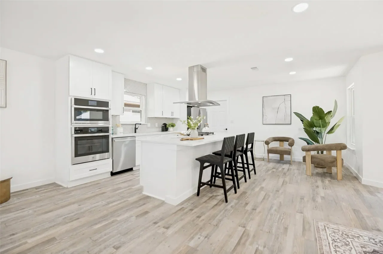 Open white kitchen and dining area with stainless appliances, a center island, recessed lighting, and light wood-look flooring in Lower Greenville, Dallas, Texas.