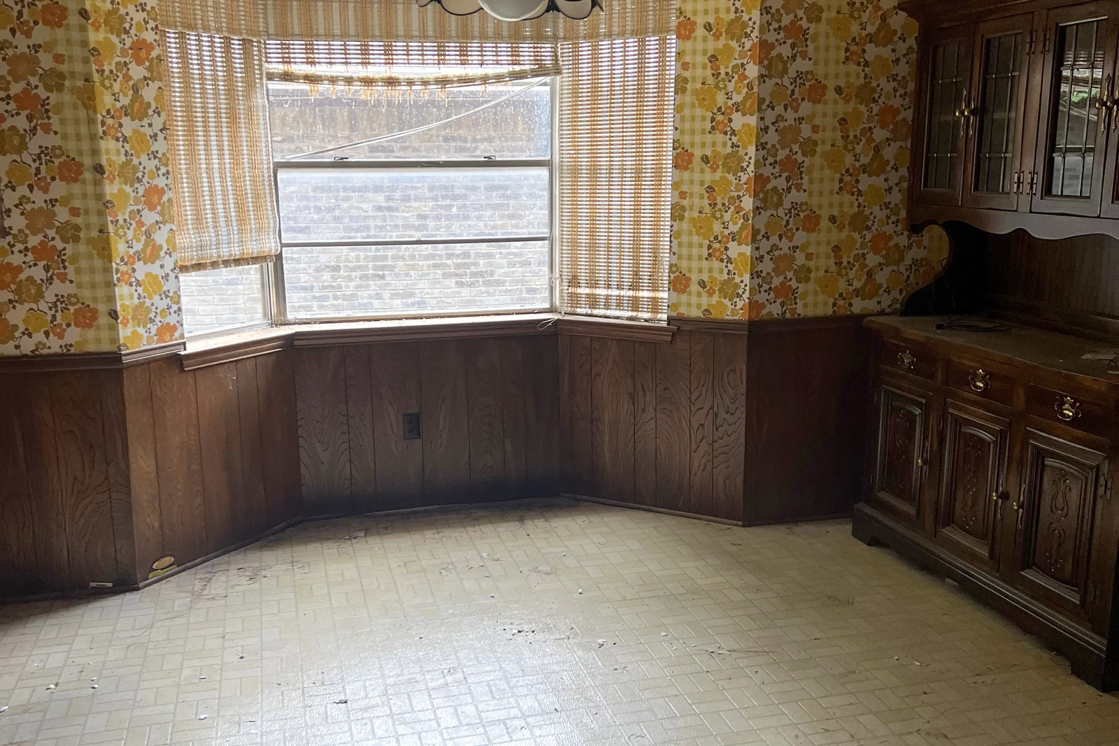 The Plano dining room before renovation, with patterned wallpaper, dark built-in cabinetry and a bare tile floor.
