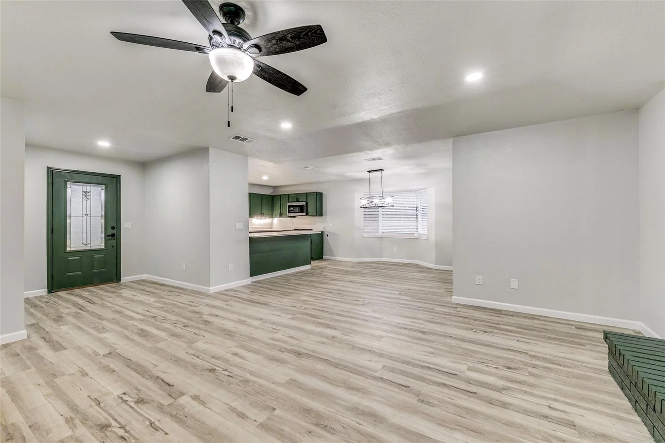 Whole-home view connecting the open living area to the deep green kitchen with light wood-look flooring and recessed lighting in Plano, Texas.