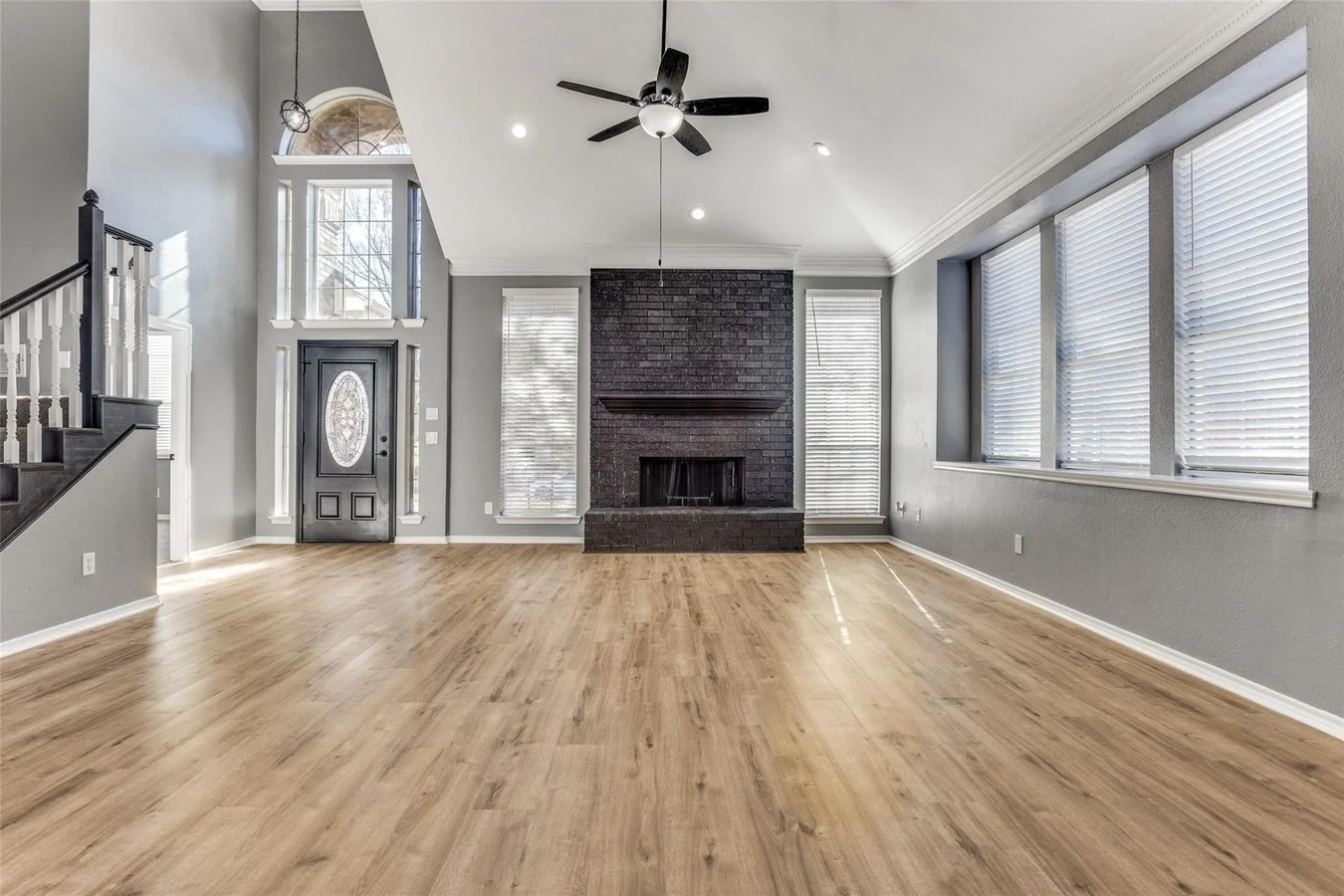 Living room with fresh gray paint, light wood flooring, black fireplace, tall entry windows, and vaulted ceiling in Rowlett, Texas.