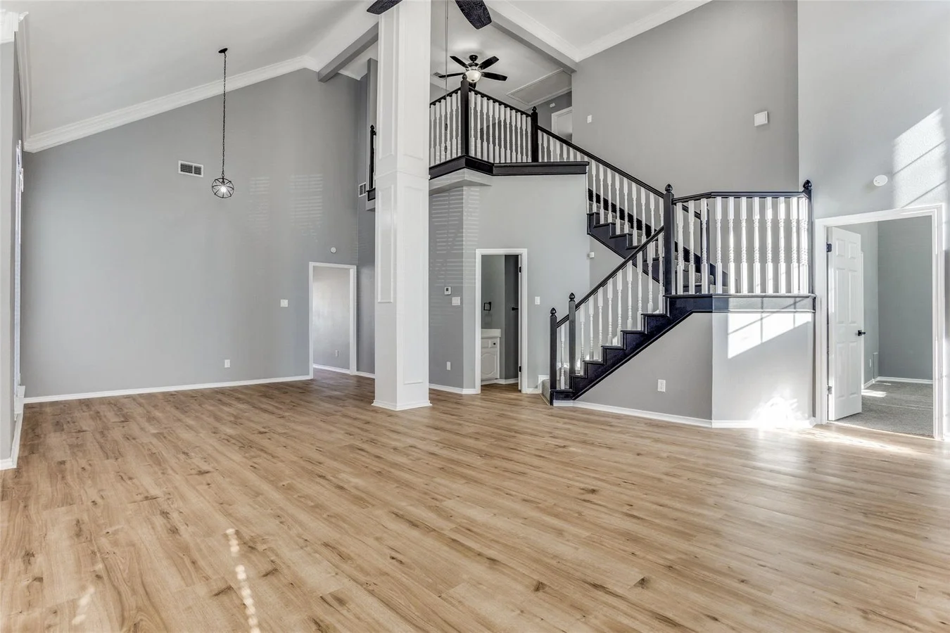 Two-story foyer and open living area with light wood flooring, black stair railings, gray walls, and modern lighting in Rowlett, Texas.